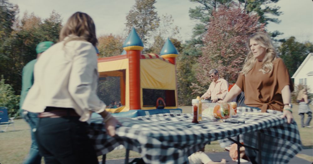 A family setting a long table in a backyard