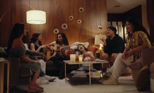 A group in a living room, one playing guitar