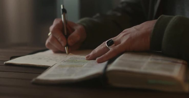 A hand writing notes beside an open Bible