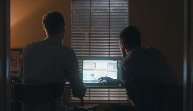 Two men at a desk at night, lit by a monitor