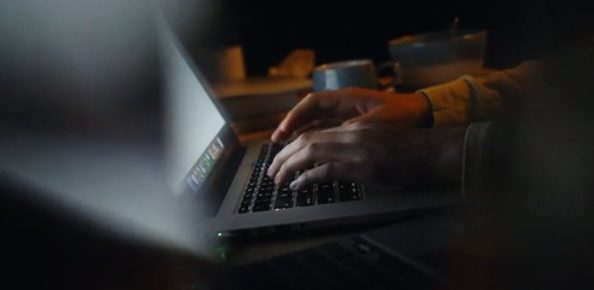 Hands typing on a laptop keyboard in the dark